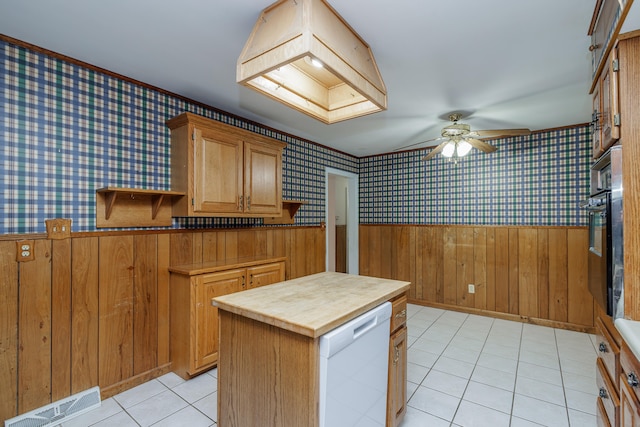 kitchen featuring ceiling fan, light tile patterned flooring, wood walls, white dishwasher, and a kitchen island