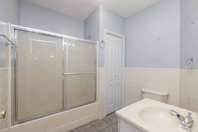 full bathroom with sink, tile patterned flooring, a textured ceiling, combined bath / shower with glass door, and tile walls