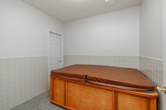 interior space with a textured ceiling, tile patterned flooring, and tile walls