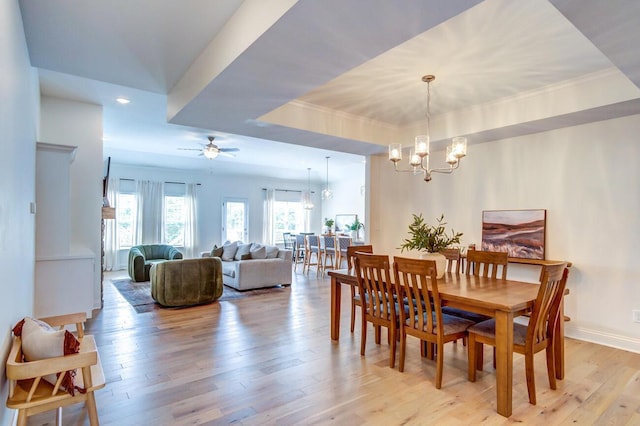 dining room featuring ceiling fan with notable chandelier, a tray ceiling, and light hardwood / wood-style flooring