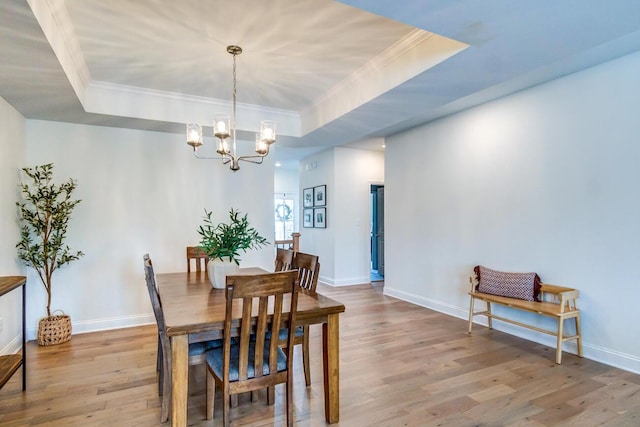 dining area with a raised ceiling, light wood-type flooring, crown molding, and an inviting chandelier