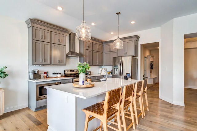 kitchen with a kitchen bar, wall chimney exhaust hood, stainless steel appliances, sink, and hanging light fixtures