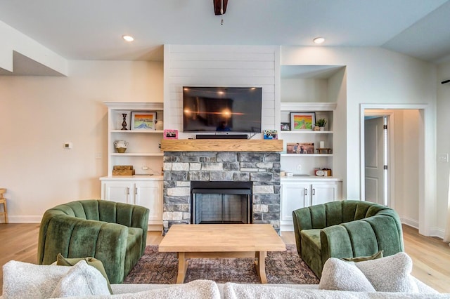 living room featuring a stone fireplace, built in features, light hardwood / wood-style floors, and vaulted ceiling