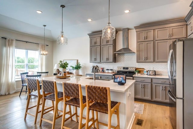 kitchen with a kitchen bar, appliances with stainless steel finishes, sink, wall chimney range hood, and decorative light fixtures