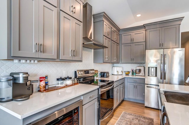 kitchen with gray cabinets, wall chimney range hood, stainless steel appliances, and vaulted ceiling