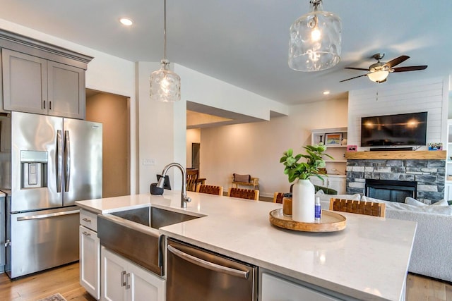 kitchen with sink, a stone fireplace, hanging light fixtures, and appliances with stainless steel finishes