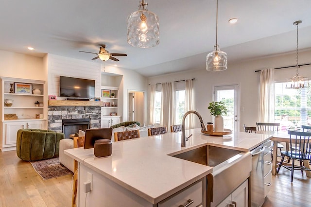 kitchen featuring a center island with sink, white cabinets, sink, hanging light fixtures, and a fireplace