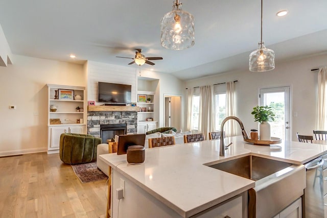 kitchen featuring stainless steel dishwasher, sink, decorative light fixtures, a stone fireplace, and an island with sink