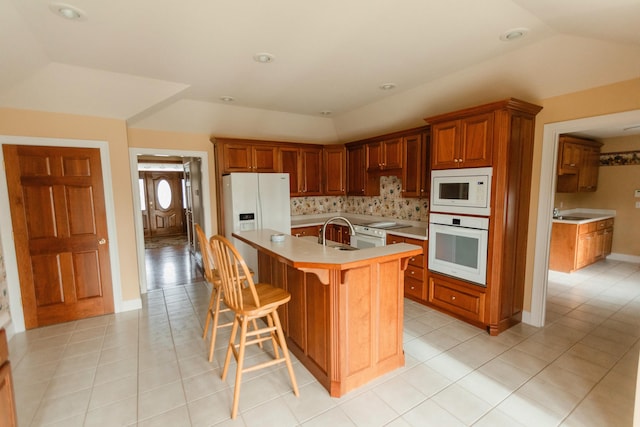 kitchen featuring sink, white appliances, a breakfast bar area, a center island with sink, and light tile patterned flooring