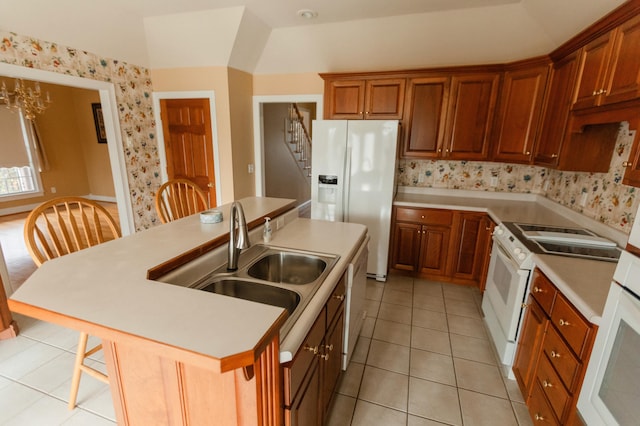 kitchen with sink, lofted ceiling, white appliances, a kitchen bar, and a center island with sink