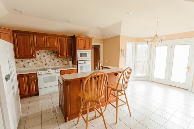 kitchen with an inviting chandelier, backsplash, decorative light fixtures, white appliances, and a center island with sink