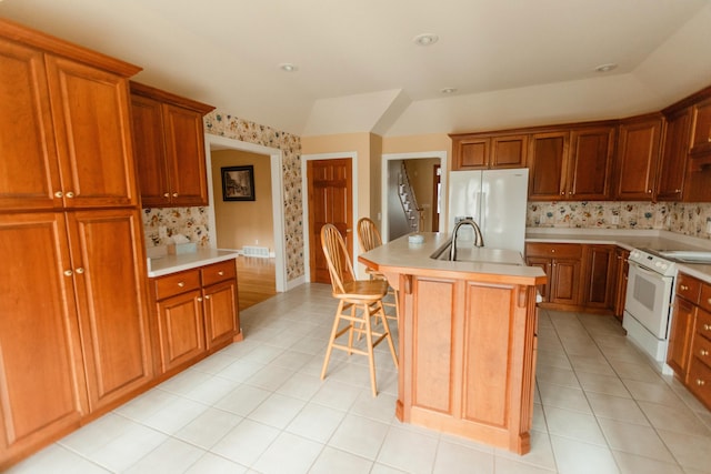 kitchen featuring sink, a kitchen breakfast bar, refrigerator with ice dispenser, white range with electric cooktop, and a center island with sink