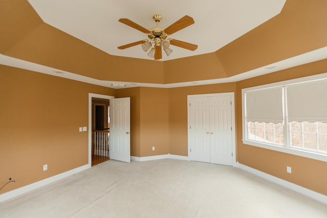 unfurnished bedroom with light carpet, a tray ceiling, a closet, and ceiling fan