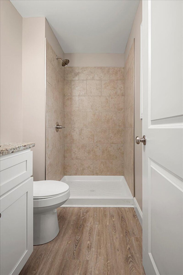 bathroom with a tile shower, hardwood / wood-style floors, vanity, and toilet