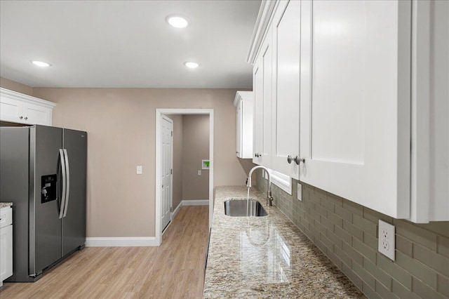 kitchen featuring white cabinetry, sink, light stone counters, stainless steel fridge, and light hardwood / wood-style floors