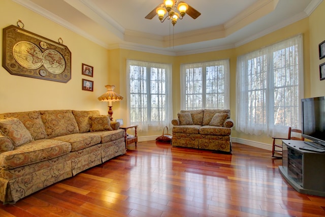 living room with a wood stove, ceiling fan, a raised ceiling, crown molding, and wood-type flooring