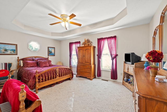 carpeted bedroom with a raised ceiling, multiple windows, and ceiling fan