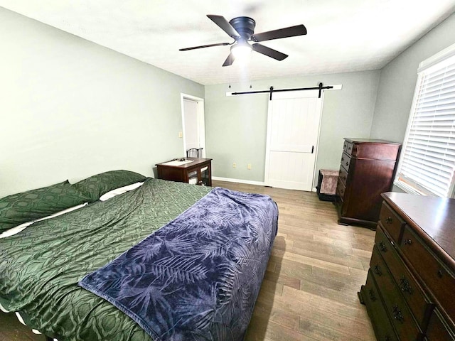 bedroom featuring hardwood / wood-style flooring, ceiling fan, and a barn door