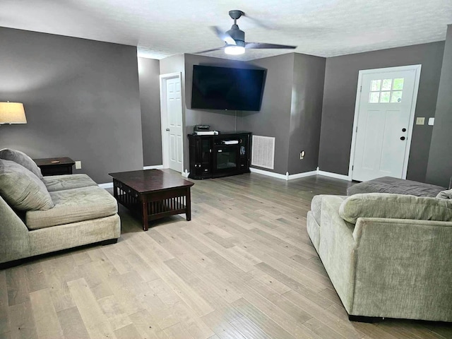 living room with a textured ceiling, light wood-type flooring, and ceiling fan