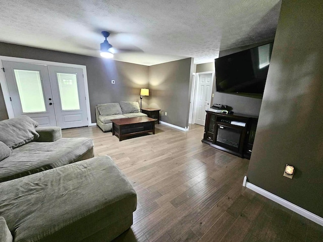 living room featuring french doors, ceiling fan, hardwood / wood-style floors, and a textured ceiling