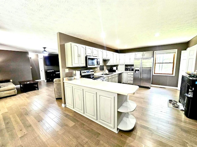 kitchen with sink, kitchen peninsula, light wood-type flooring, white cabinetry, and stainless steel appliances