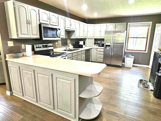 kitchen featuring kitchen peninsula, stainless steel appliances, sink, wood-type flooring, and white cabinetry