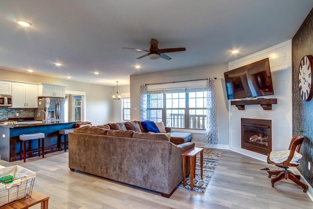 living room featuring a fireplace, light hardwood / wood-style floors, and ceiling fan with notable chandelier