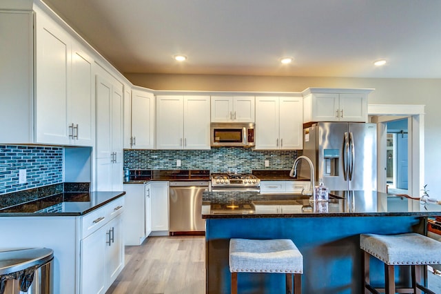 kitchen featuring white cabinets, appliances with stainless steel finishes, light hardwood / wood-style flooring, and dark stone countertops