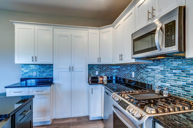 kitchen with white cabinets, appliances with stainless steel finishes, backsplash, and wood-type flooring