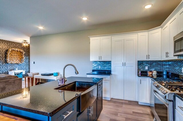 kitchen featuring dark stone counters, sink, appliances with stainless steel finishes, light hardwood / wood-style floors, and white cabinetry