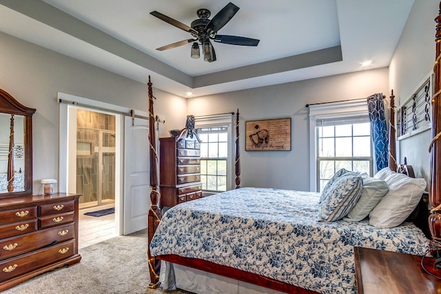 carpeted bedroom featuring a raised ceiling, multiple windows, ceiling fan, and ensuite bath