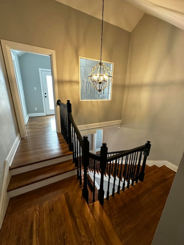 stairway featuring hardwood / wood-style flooring, a notable chandelier, and lofted ceiling