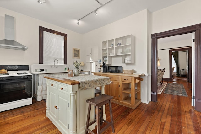 kitchen with a center island, dark wood-type flooring, wall chimney range hood, a breakfast bar area, and white gas range oven