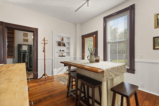 kitchen with built in shelves, rail lighting, dark wood-type flooring, a kitchen breakfast bar, and black refrigerator