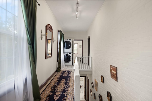 hall with stacked washer / drying machine, light tile patterned floors, brick wall, and track lighting