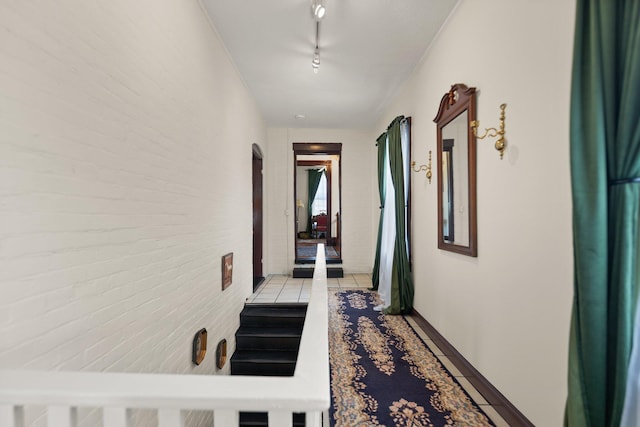 hallway featuring light tile patterned floors, brick wall, and rail lighting