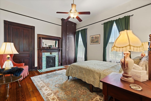 bedroom with multiple windows, ceiling fan, a stone fireplace, and dark hardwood / wood-style floors