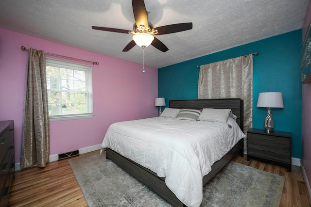 bedroom with ceiling fan, wood-type flooring, and a textured ceiling