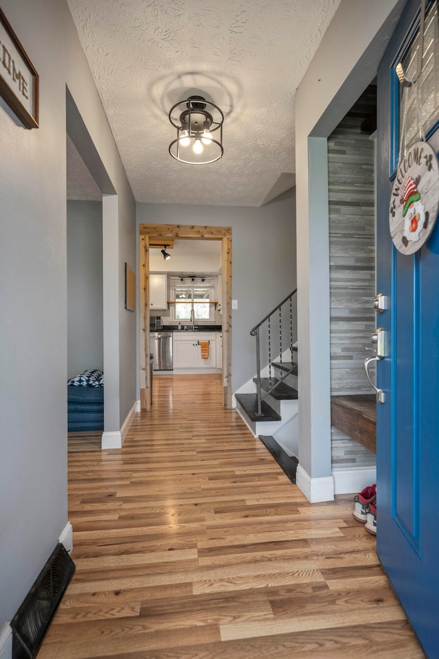 entryway with a textured ceiling, light hardwood / wood-style floors, wooden walls, and sink