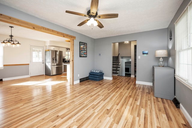 unfurnished living room featuring ceiling fan with notable chandelier, light hardwood / wood-style floors, and a textured ceiling