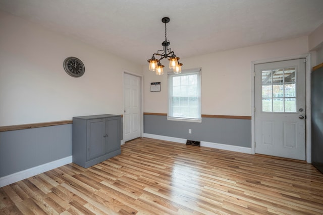 unfurnished dining area featuring a notable chandelier and light wood-type flooring