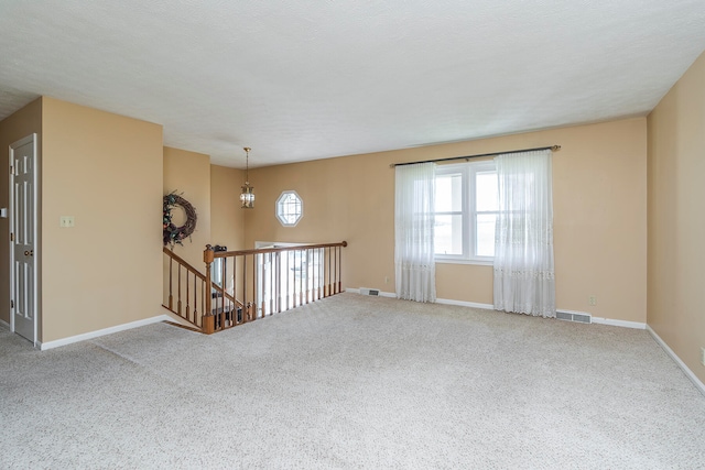 unfurnished room with carpet flooring, a textured ceiling, and an inviting chandelier