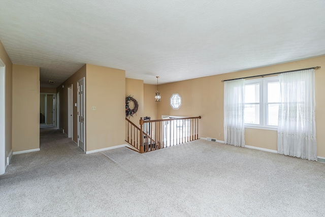 carpeted empty room featuring a notable chandelier and a textured ceiling