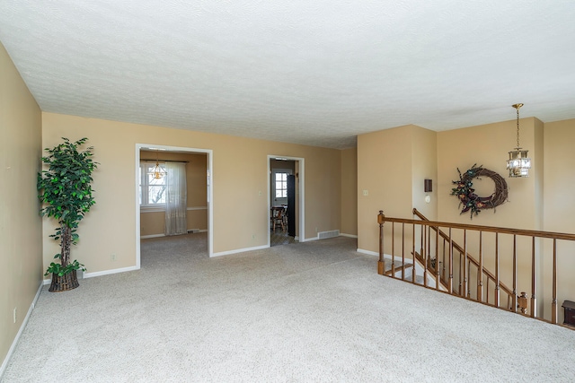 empty room with carpet, a textured ceiling, and a chandelier