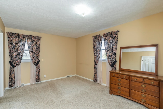 unfurnished bedroom featuring light colored carpet, a textured ceiling, and multiple windows