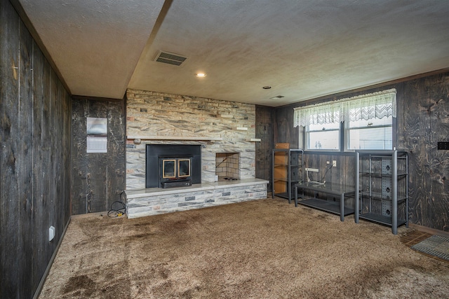 unfurnished living room featuring a stone fireplace, wooden walls, carpet, and a textured ceiling