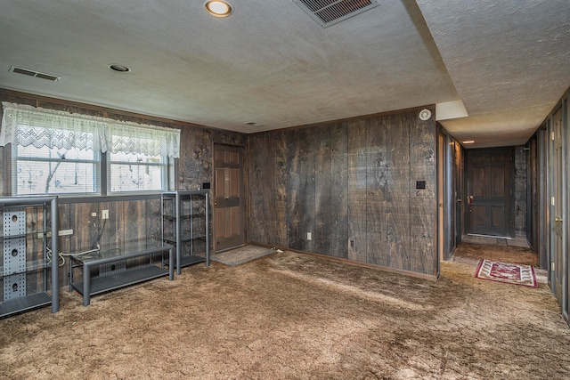 spare room with carpet flooring, a textured ceiling, and wooden walls