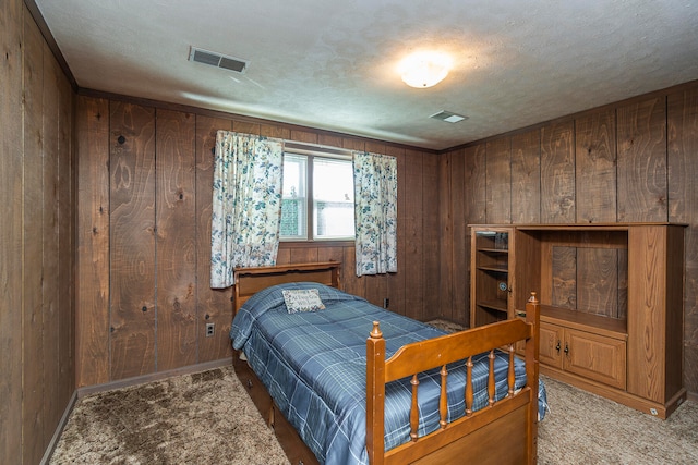 bedroom with carpet, a textured ceiling, and wooden walls