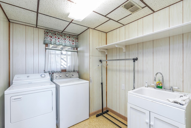 clothes washing area featuring cabinets, wood walls, washing machine and dryer, and sink