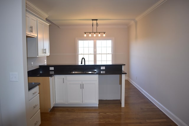 kitchen featuring a sink, crown molding, a peninsula, dark countertops, and white cabinets